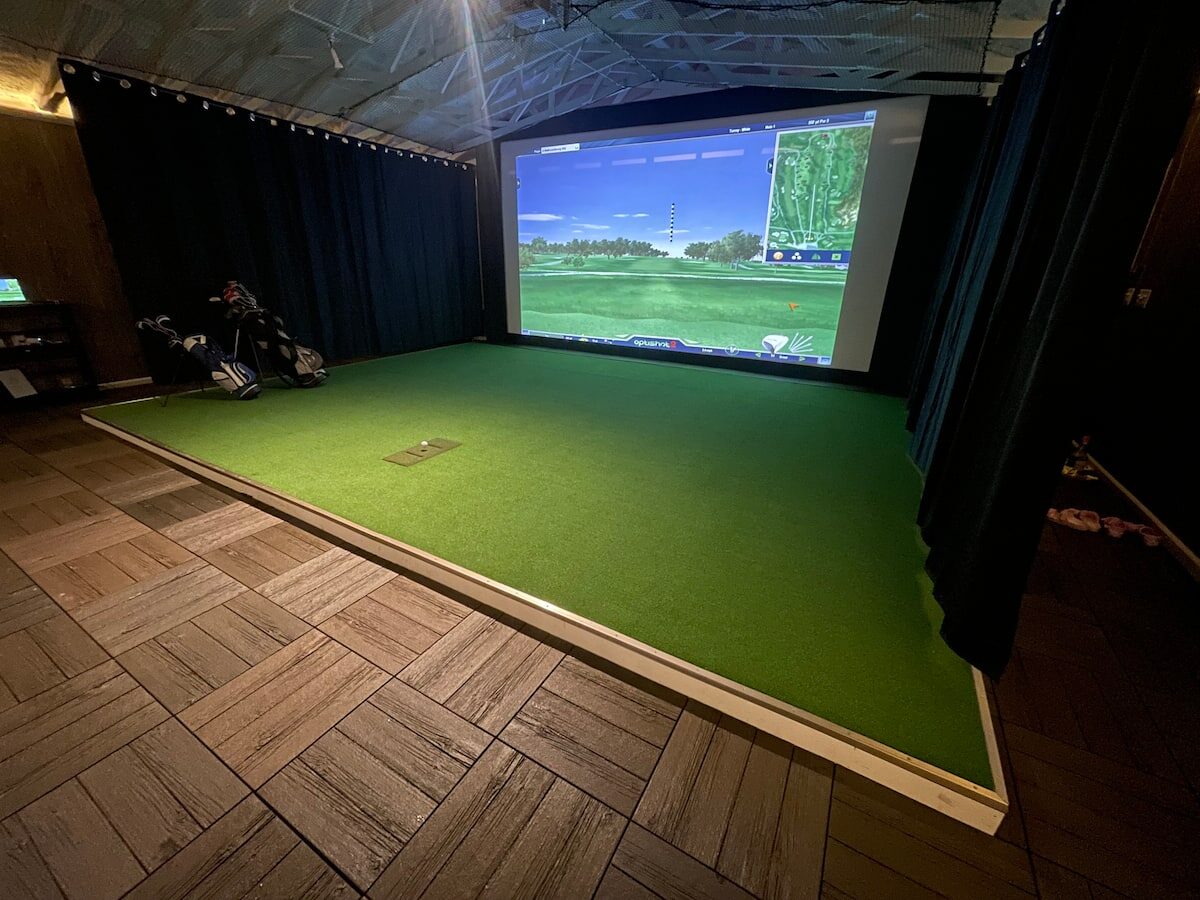 Indoor golf simulator with turf and a large course projection.