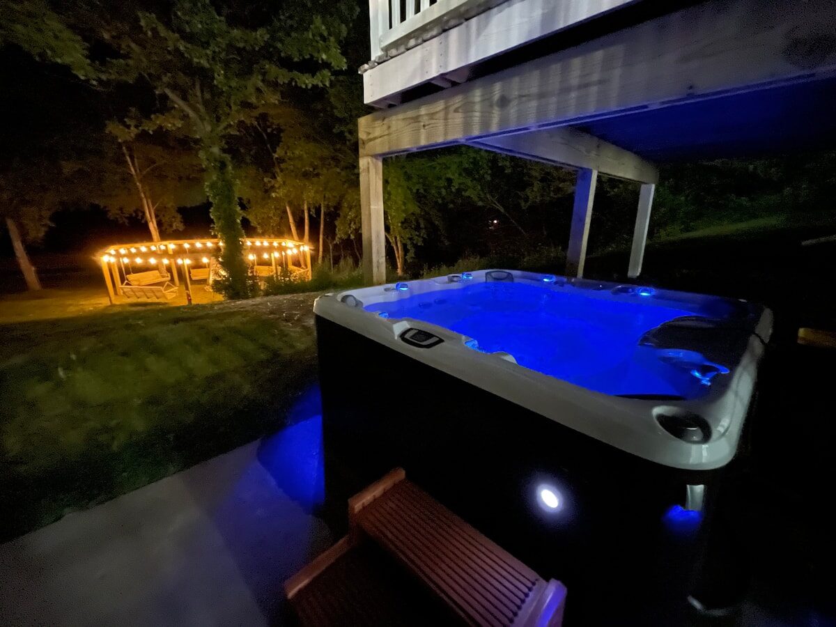 Hot tub glowing blue at night next to a lit gazebo.