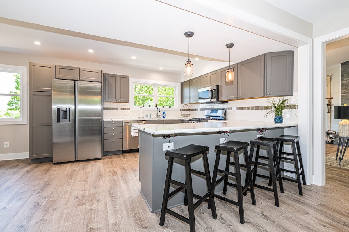 Main kitchen with gray cabinets, island seating, and stainless appliances.